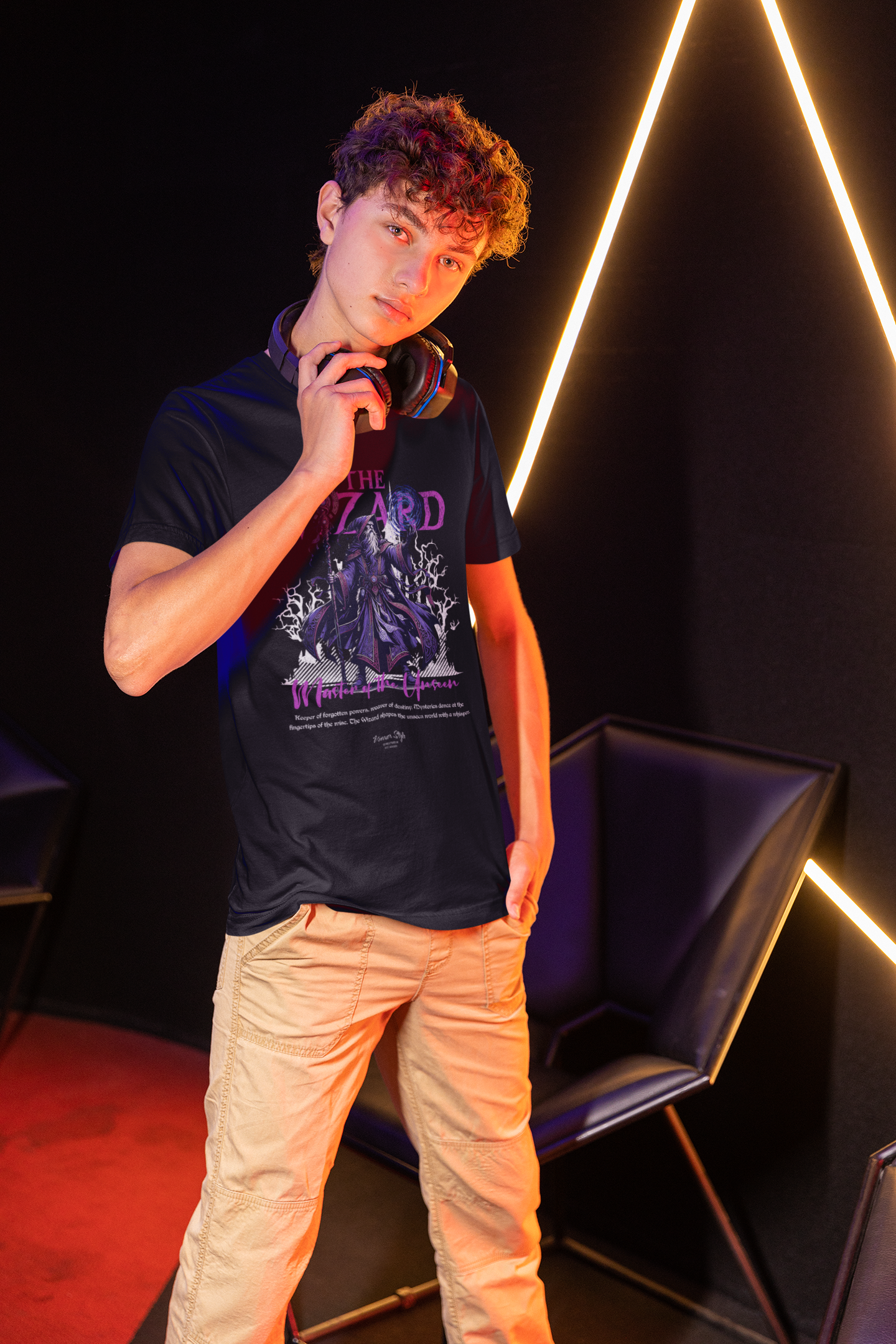 Young man in a dimly lit, neon-accented room, wearing THE WIZARD t-shirt. He stands confidently with headphones around his neck, glowing purple lightning from the wizard design reflecting the ambient mood.