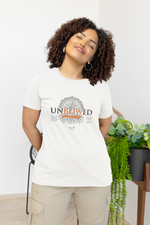 A serene woman in a white UNBOWED t-shirt stands indoors with her eyes closed and a soft smile, exuding calm confidence. The shirt features a large tree graphic with deep roots and the word “UNBOWED” boldly printed, accented in orange.