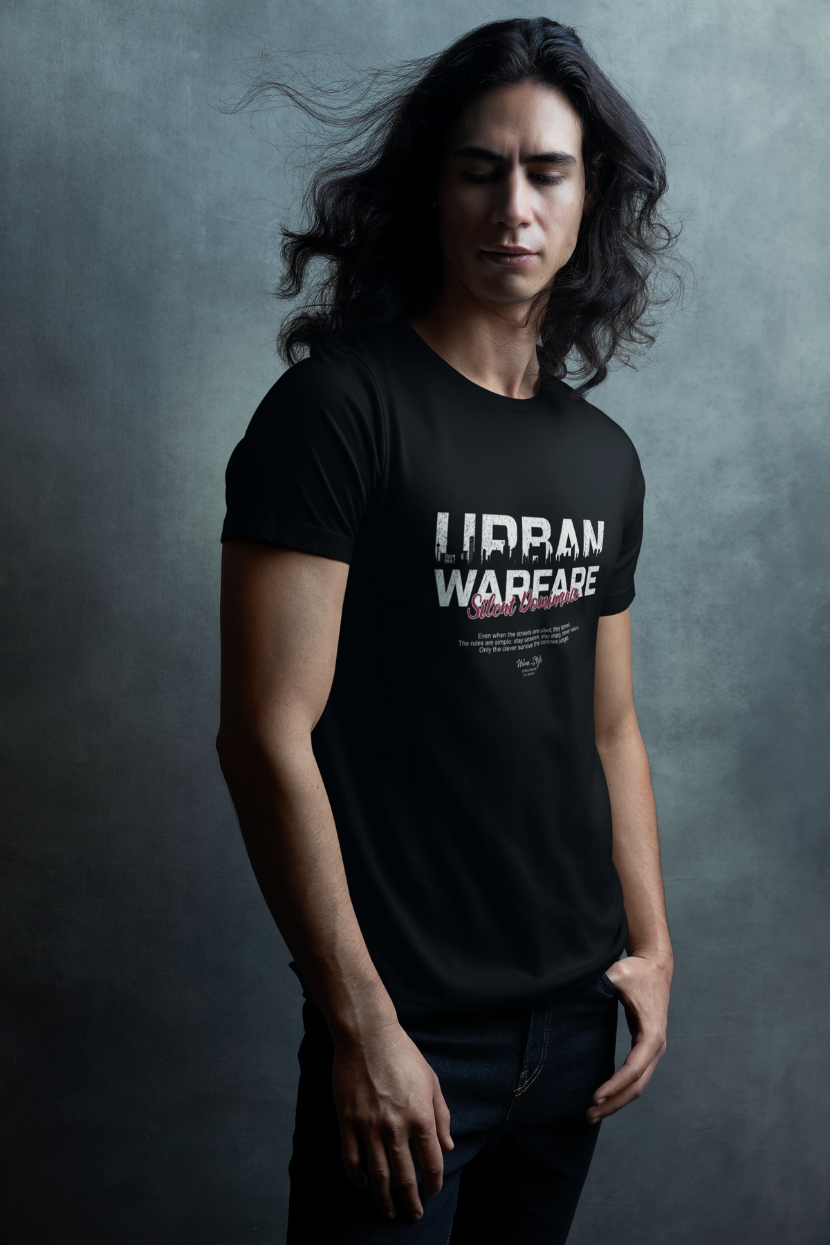 Black URBAN WARFARE t-shirt worn by a man with long flowing hair, standing in front of a textured grey wall — design includes bold white text and red "Silent Dominance" subtitle.