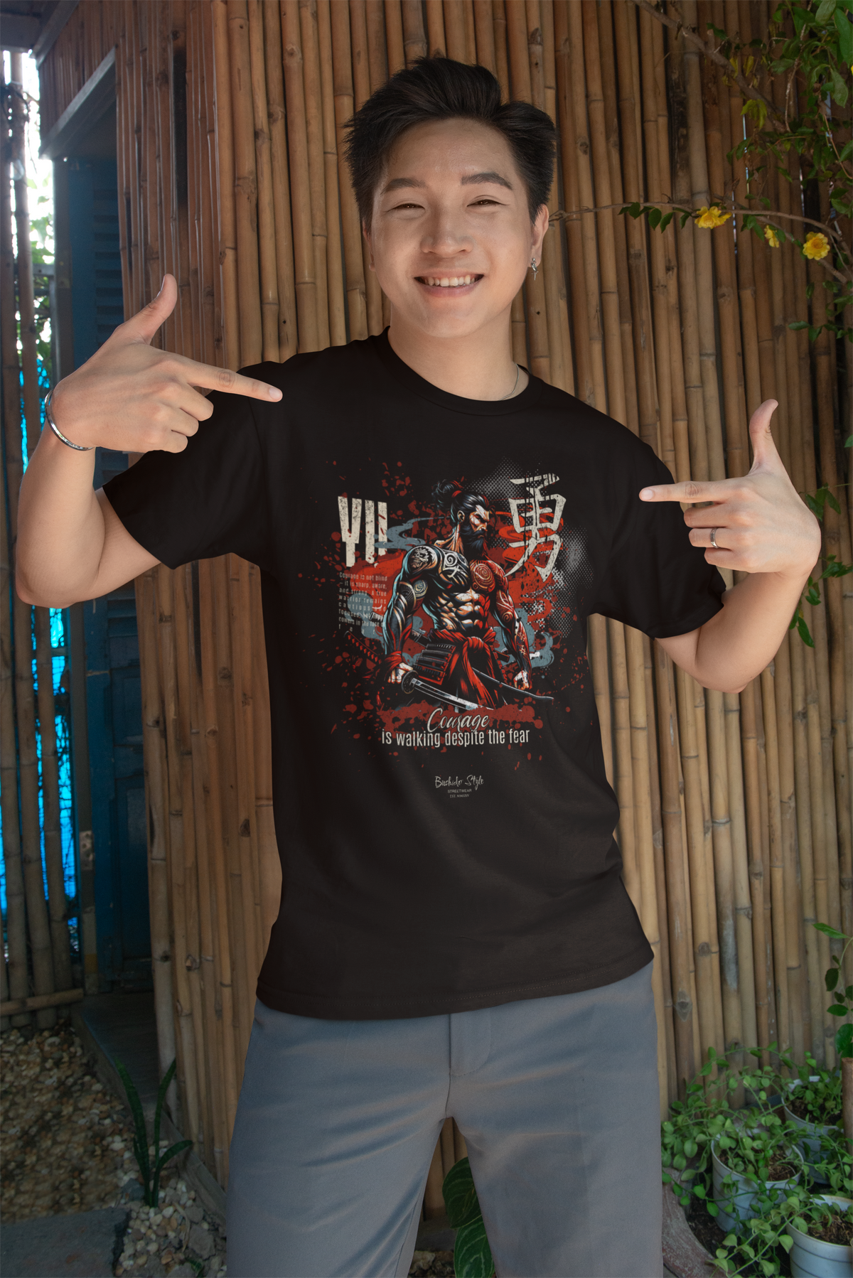 “YU” black t-shirt by KRASSWERK – lifestyle photo of man smiling confidently and pointing at Bushido-inspired courage design, with bamboo wall backdrop and natural light warmth